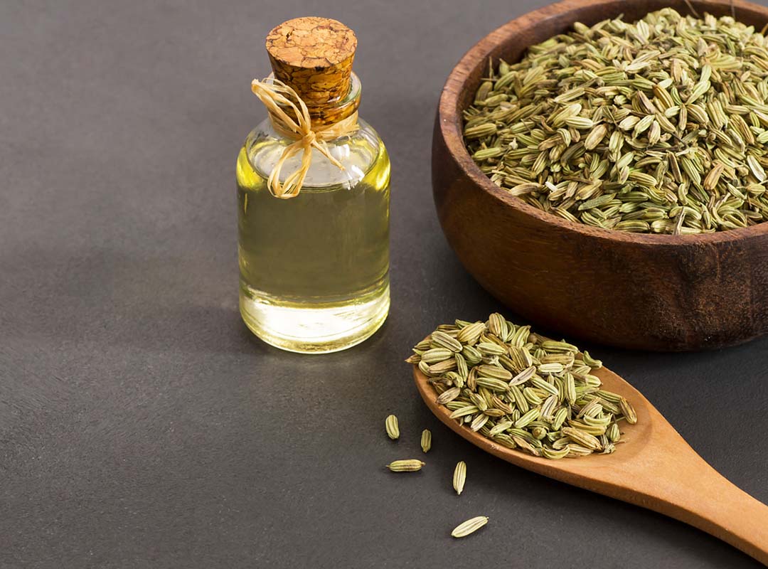 Glass bottle of fennel essential oil with fennel seeds in wooden spoon on rustic table. Herbs alternative medicine background concept